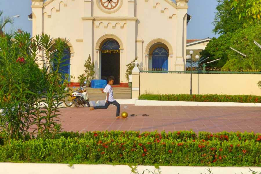Boy kicks a gold ball beside the church in Savannakhet, Laos
